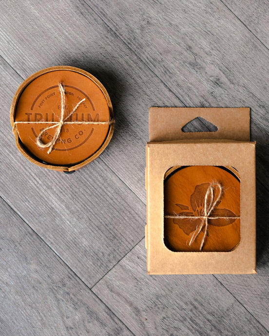 Leather coaster set with Trillium circle and flower logo in cardboard case tied with string