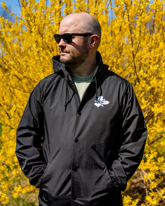 Male wearing unisex black water resistant jacket with white Trillium flower logo