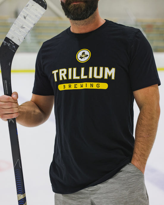 Male wearing Trillium black and gold t-shirt holding hockey stick
