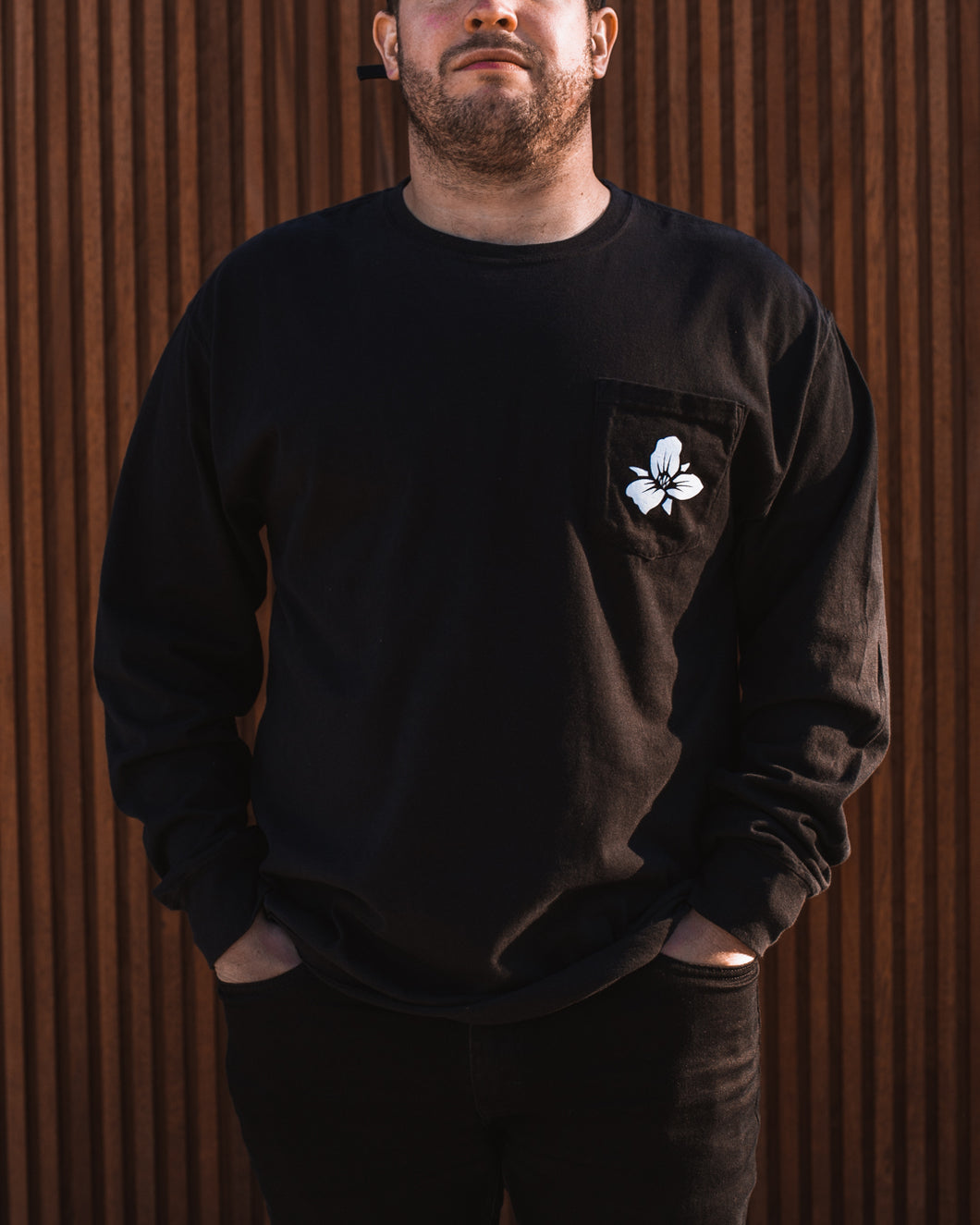 Male wearing unisex black Trillium flower logo long sleeve t-shirt