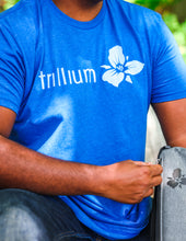 Load image into Gallery viewer, blue t-shirt with Trillium flower logo and horizontal text
